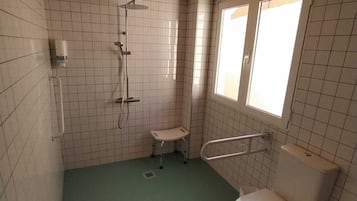 A small, tiled bathroom with a green floor, a shower, a toilet, and a window.