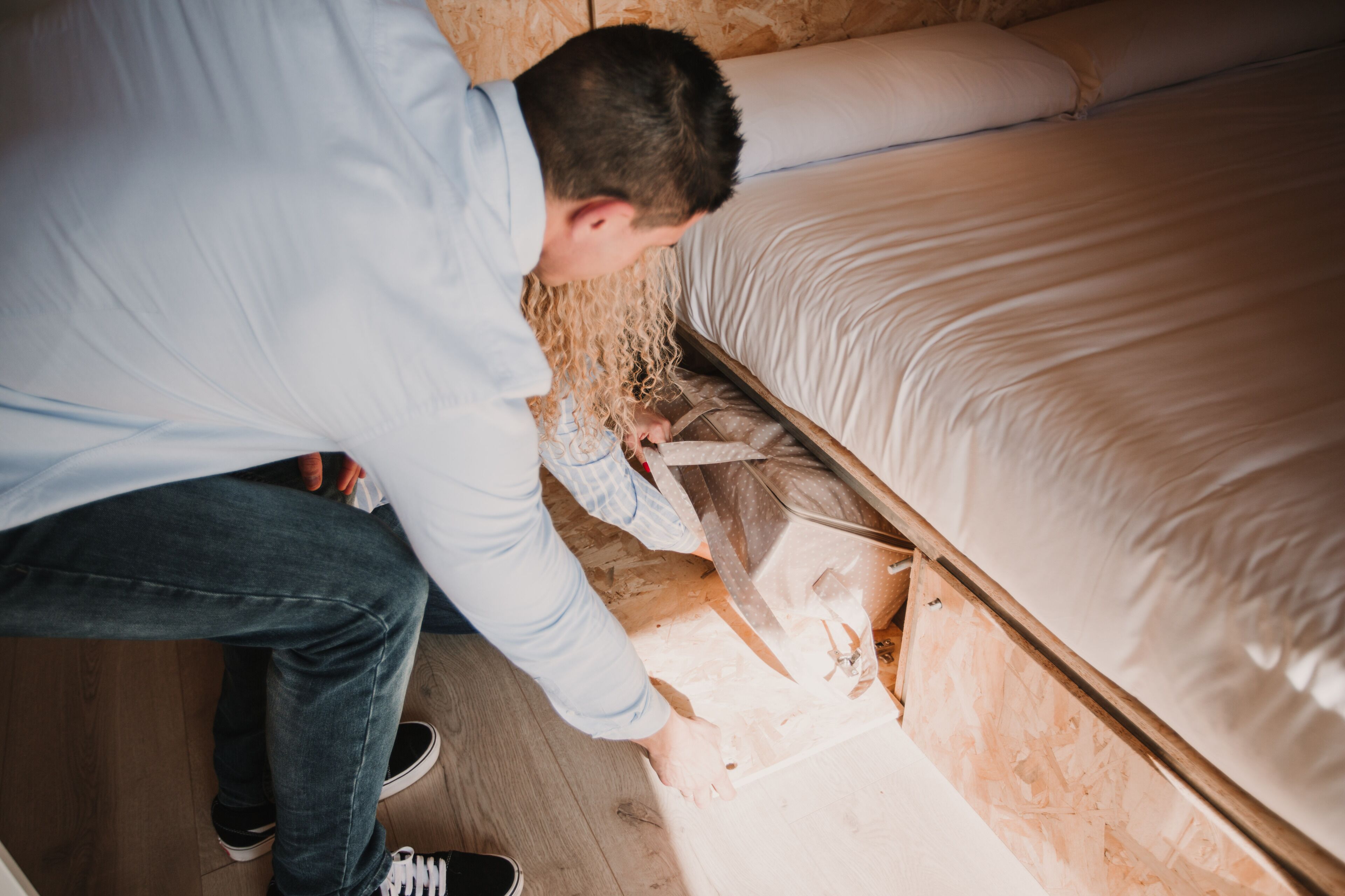 Una persona trabajando sobre un piso de madera en una habitación con una cama y un cabecero de madera.
