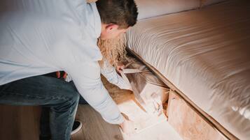 Una persona trabajando sobre un piso de madera en una habitación con una cama y un cabecero de madera.