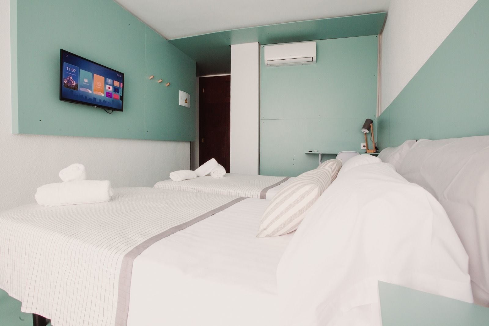 Quarto de hotel com duas camas, televisão de tela plana fixada na parede e aparelho de ar condicionado na parede.