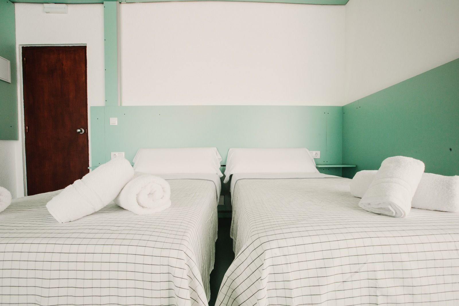 A hotel room with two beds, each with a striped bedspread and white pillows. There are rolled white towels on the beds.