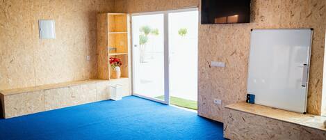 Une pièce avec une moquette bleue, des murs en bois, une porte blanche et un téléviseur fixé au mur.