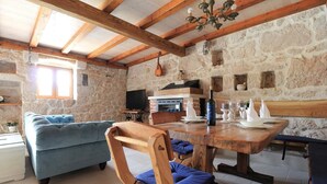 Una habitación rústica con pared de piedra, vigas de madera, un sofá azul, una mesa de comedor de madera y una chimenea.