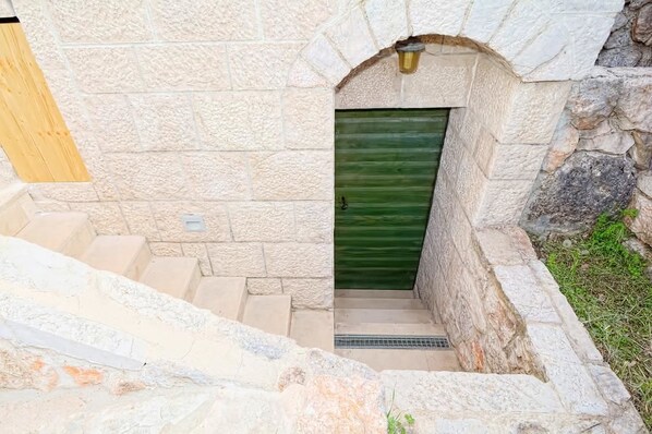 A stone staircase leading to a door with a green shutter, set against a textured stone wall.