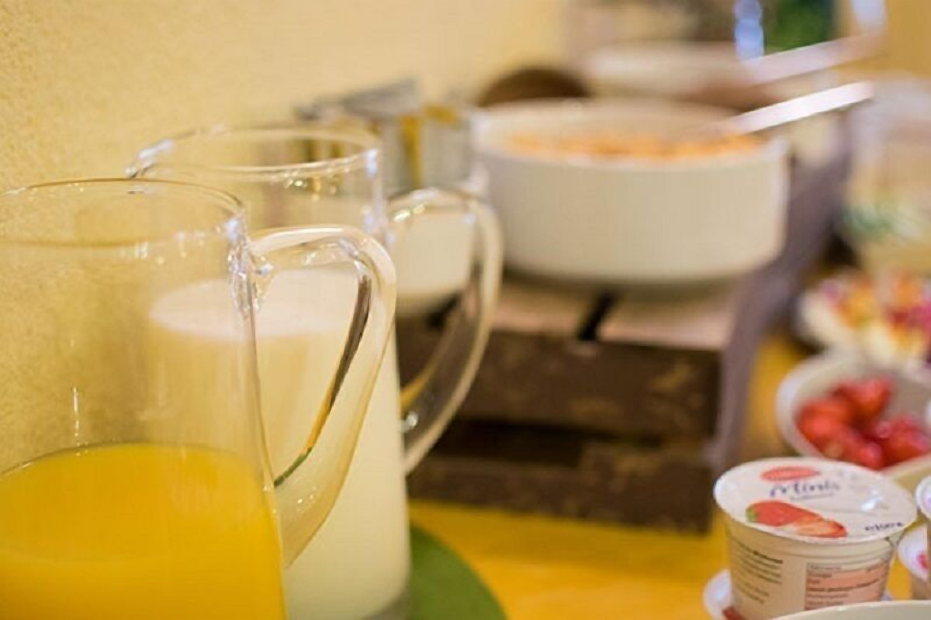 A breakfast setting with a pitcher of orange juice, a bowl of cereal, and yogurt cups.