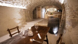 A rustic dining area with a wooden table set for two, a wine glass, and a candle. A large barrel is visible in the background, and a kitchen area with a refrigerator and sink is seen through an arched doorway. - Agriturismo Il Casanova (Baschi)