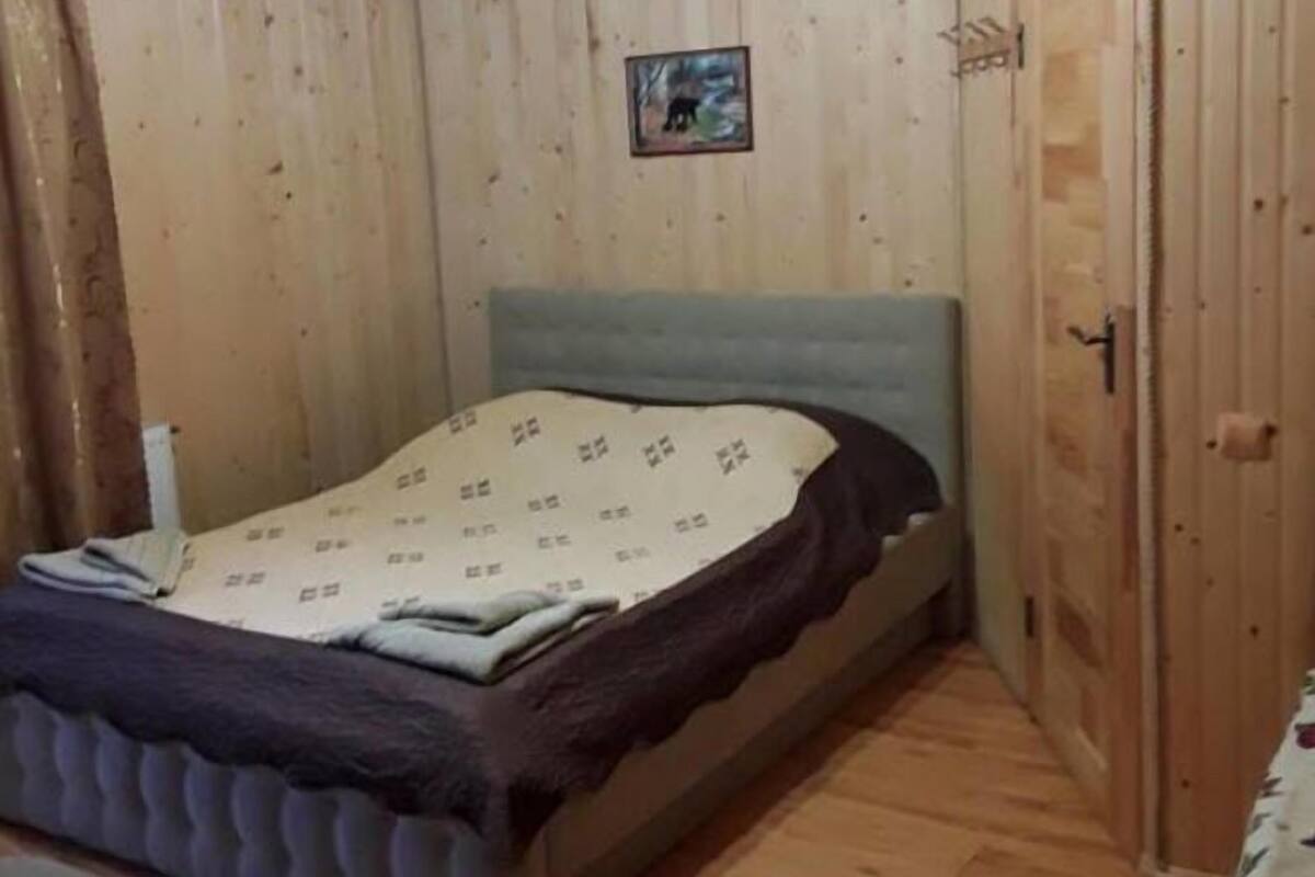 Un dormitorio con techo de madera, una cama con colcha estampada, un pequeño cuadro enmarcado en la pared y una puerta de madera.