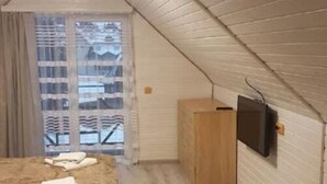 A small, sloped-roofed room with a bed, a wooden wardrobe, and a television mounted on the wall. - Saduba Perluna Bukovel (Bukovel)