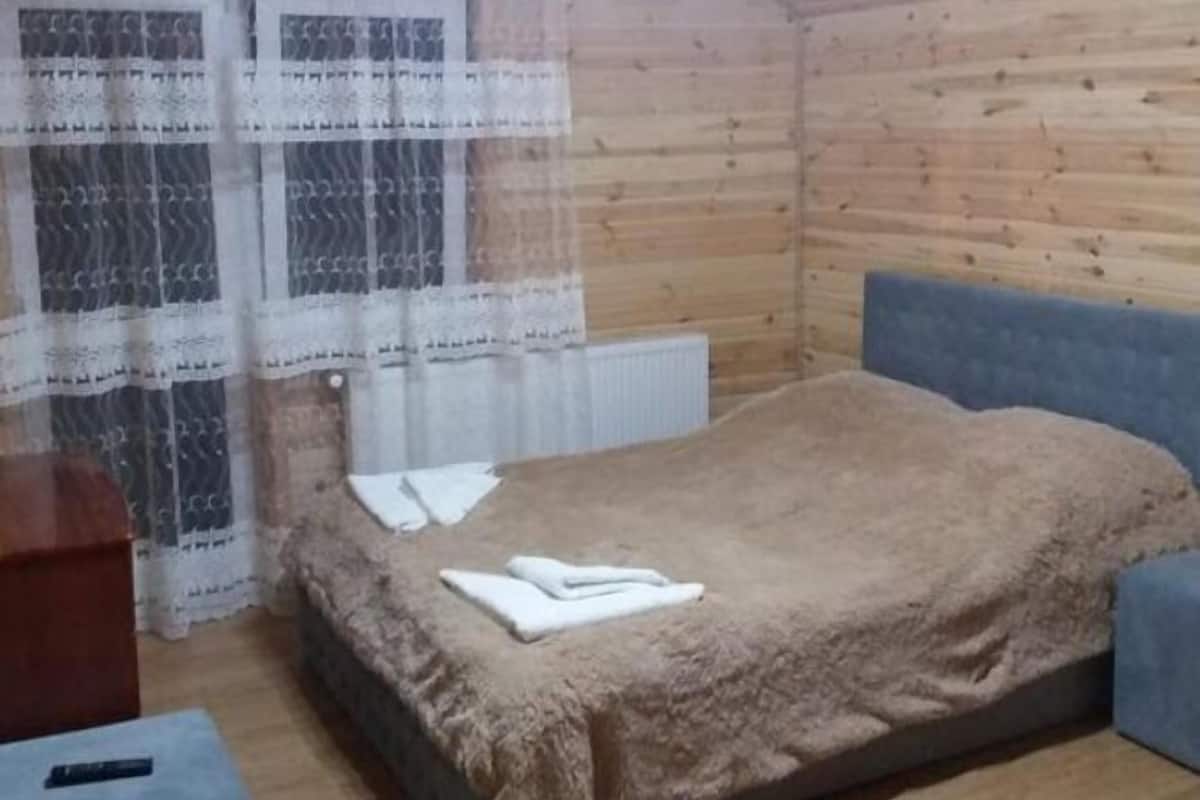 Una habitación pequeña y acogedora con una cama individual, una mesita y un ventanal con cortinas.