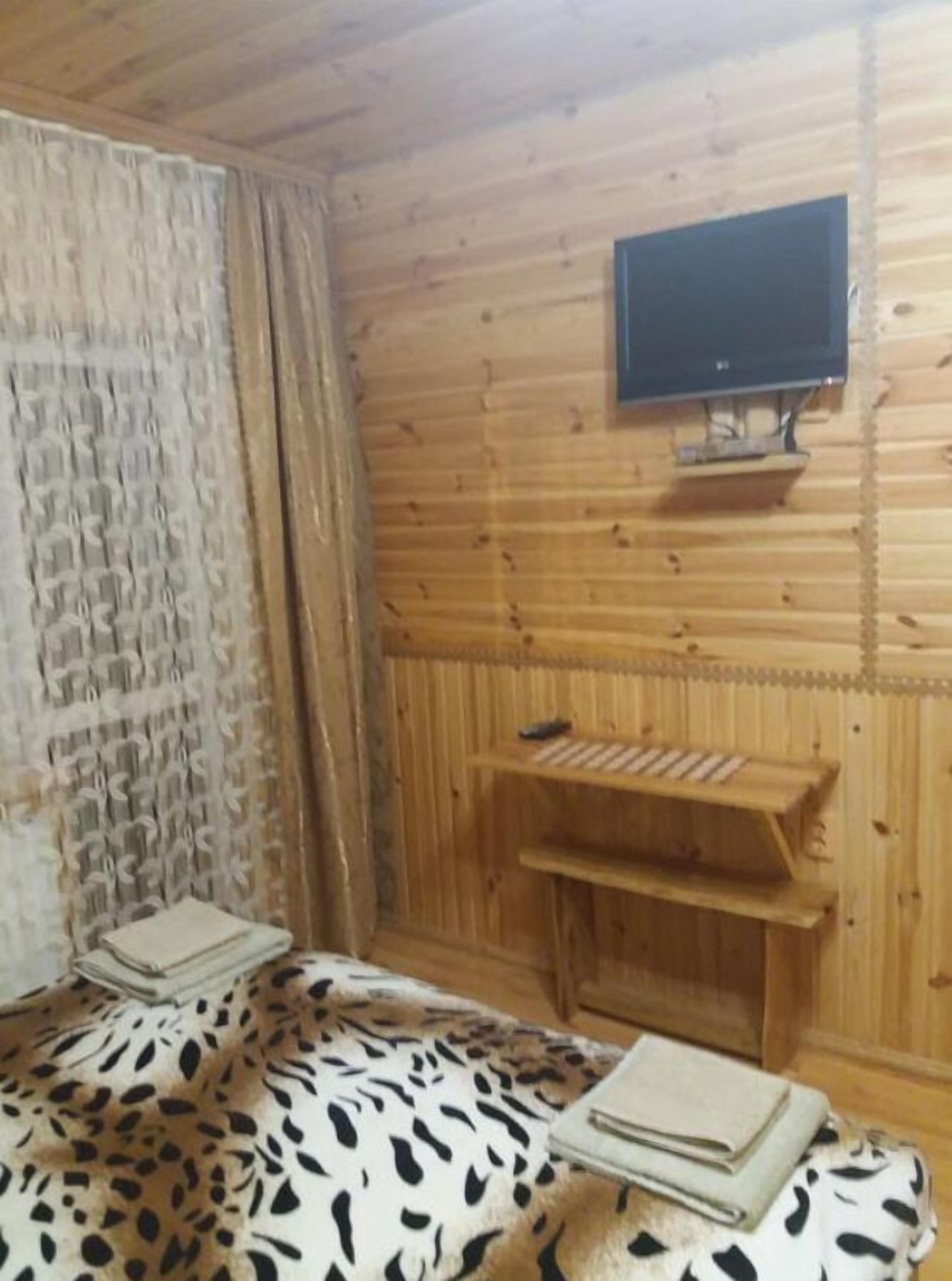 Una habitación con paneles de madera, una cama, un televisor montado en la pared y un pequeño estante de madera.