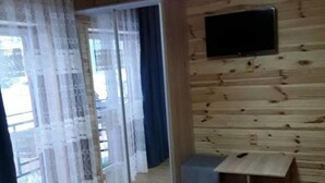 A room with wooden walls, a sliding glass door, a flat-screen TV mounted on the wall, and a small wooden bench. - Saduba Perluna Bukovel (Bukovel)