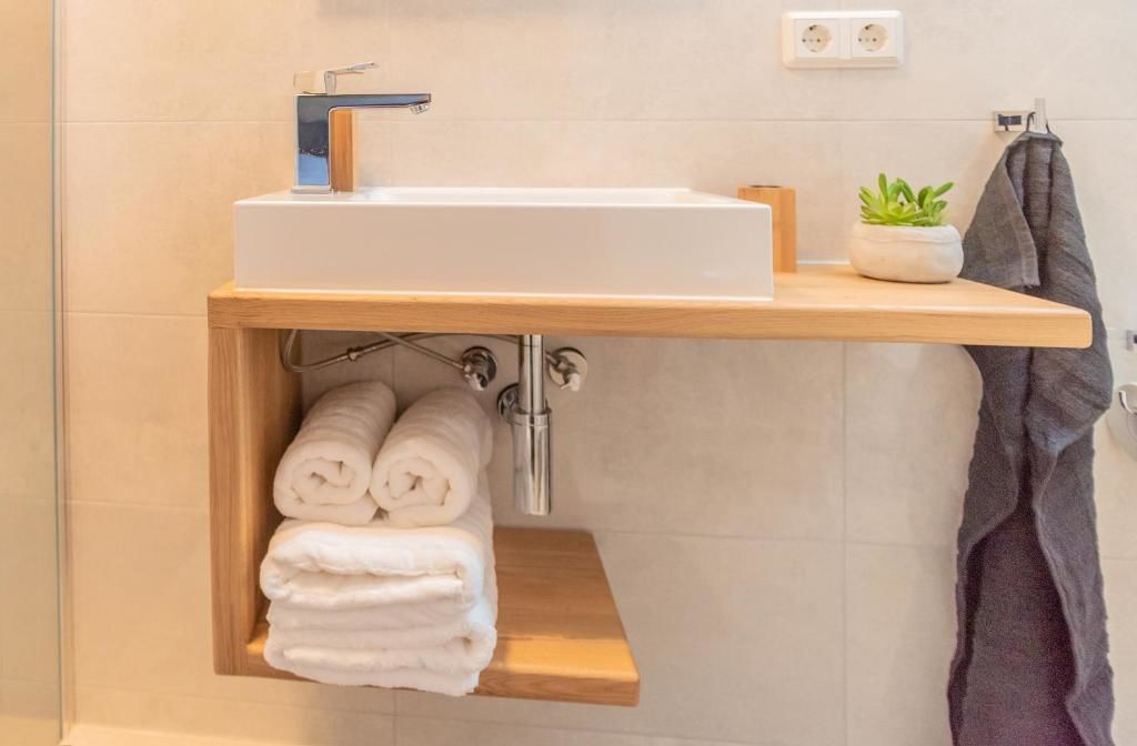 Une salle de bain avec un lavabo blanc, une étagère en bois en dessous et un porte-serviettes sur la droite.
