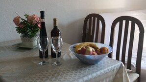 A dining table with a white tablecloth, a bowl of fruit, a bottle of wine, and two glasses. There is a vase with flowers on the left and a painting of a flower on the wall. - Apartments Mirjana (Dugi Rat)