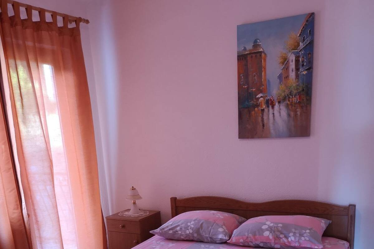 A bedroom with a wooden bed, a nightstand, a painting on the wall, and a window with curtains.