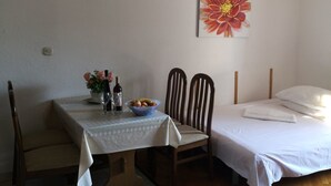 A room with a bed, a dining table with chairs, a wall clock, and a flower painting. - Apartments Mirjana (Dugi Rat)