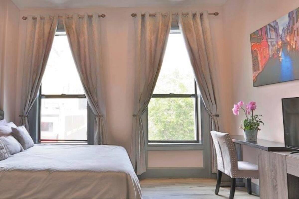 A bedroom with a bed, a desk, a chair, a potted plant, and a painting on the wall.