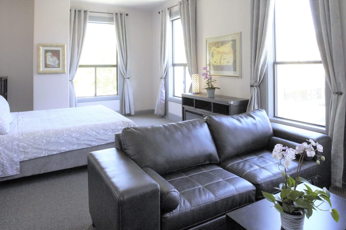 A hotel room with a bed, a sofa, a nightstand, a lamp, and a window with curtains.