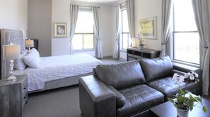 Een hotelkamer met een bed, een bank, een nachtkastje, een lamp en een raam met gordijnen.