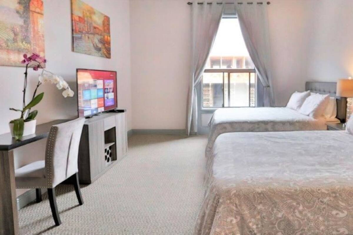 A hotel room with two beds, a desk with a computer, a TV, and a window with curtains.