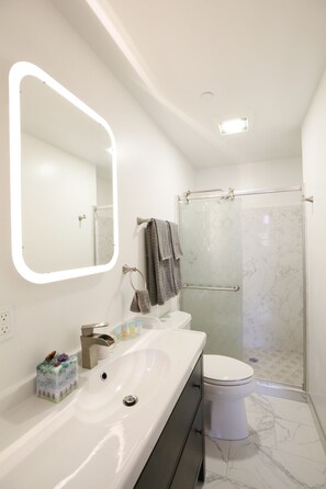 Een moderne badkamer met een grote spiegel, een wit wastafelmeubel, toilet en een douche met glazen wanden.