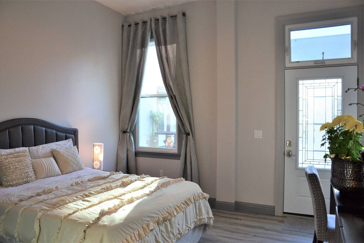A bedroom with a bed, curtains, a window, a door, and a chair with a potted plant.