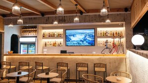 Zona de bar con sillas de mimbre, una barra con pantalla de televisión y estantes llenos de botellas.