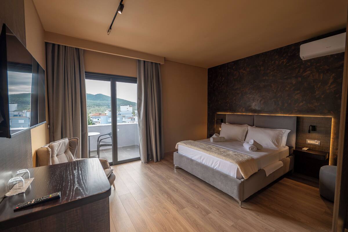 Un hotel moderno con una cama grande, un escritorio con control remoto y vistas a la ciudad desde el balcón.