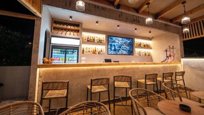 Zona de bar con sillas de mimbre, una barra con estantes llenos de botellas y una obra de arte grande en la pared.