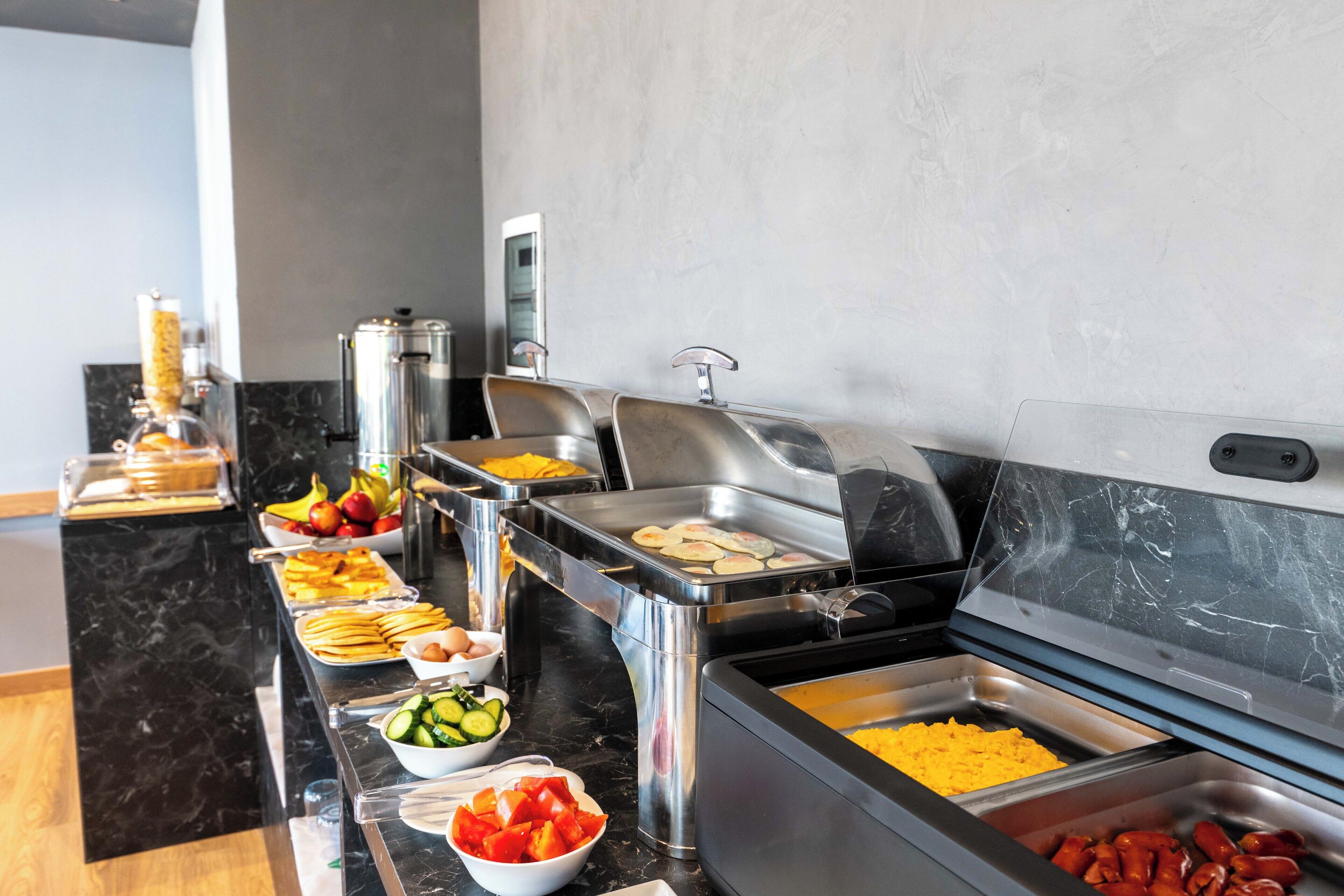 Un buffet proposant une variété de plats, notamment des fruits, des légumes et des saucisses.
