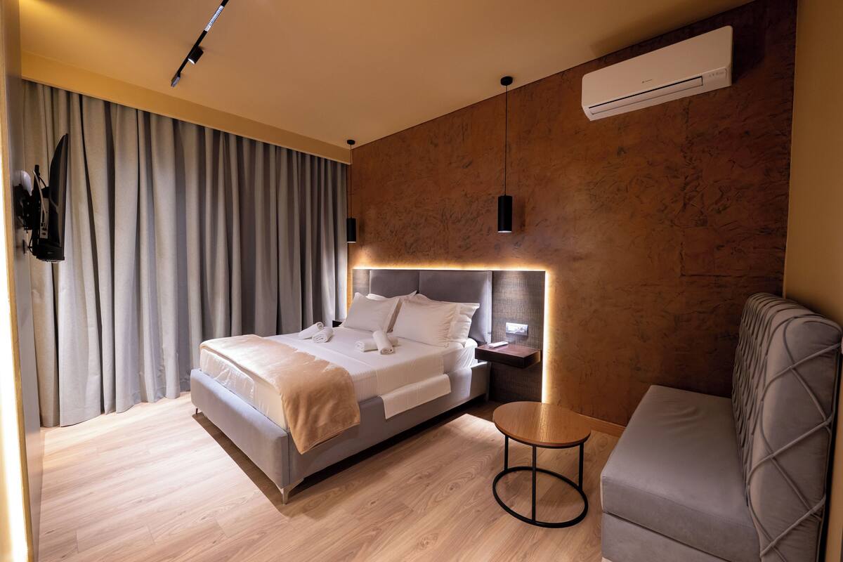 Una habitación de hotel moderna con una cama grande, una pequeña mesa redonda, un sofá y un equipo de aire acondicionado en la pared.