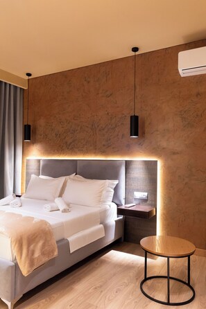 A modern hotel room with a large bed, bedside tables, a round wooden side table, and a wall-mounted air conditioning unit. - Hotel Piramida (Ksamil)