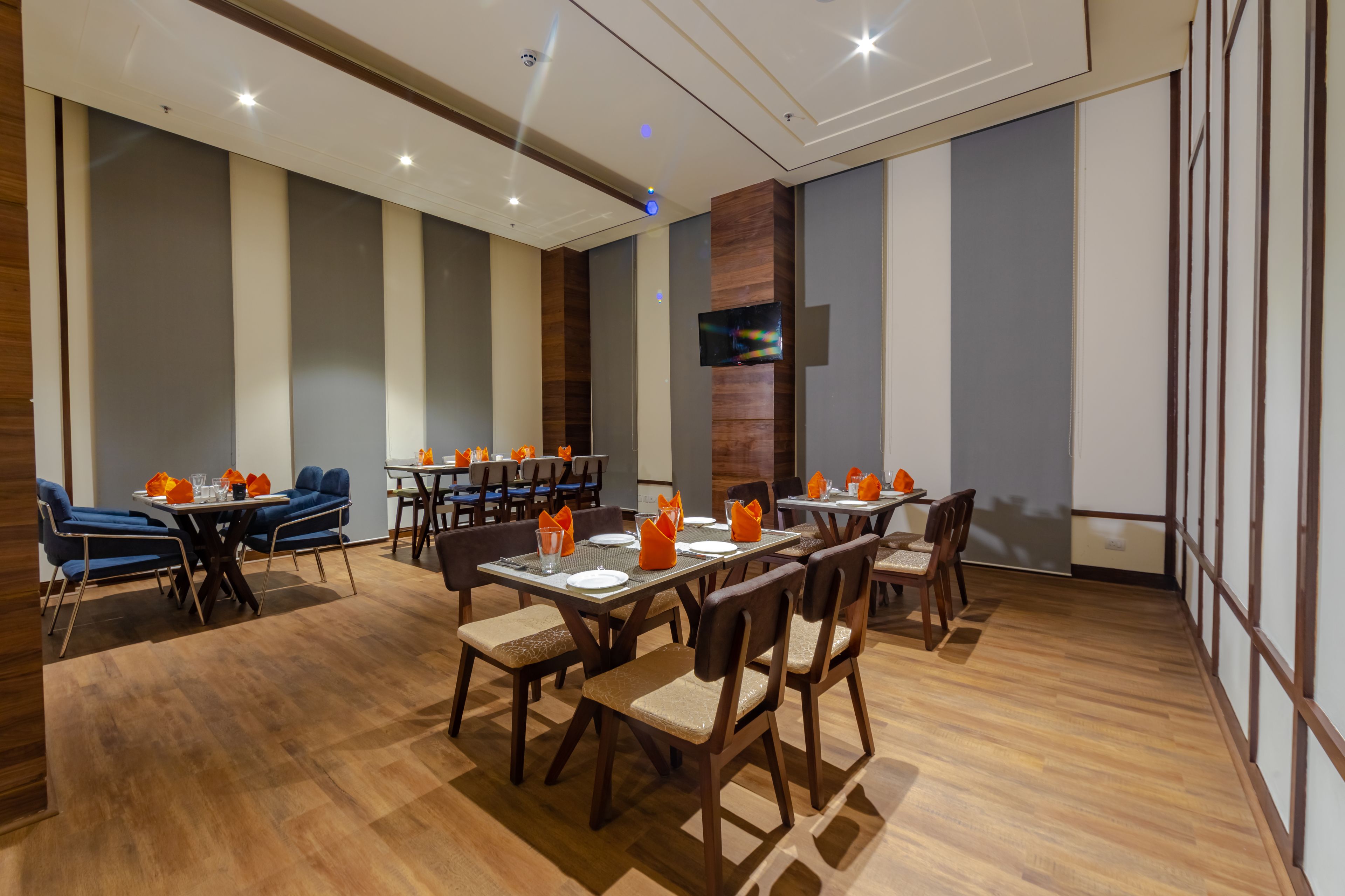 Un espace repas moderne, doté de plusieurs tables et chaises, d’un téléviseur à écran plat fixé au mur et d’un plancher en bois.