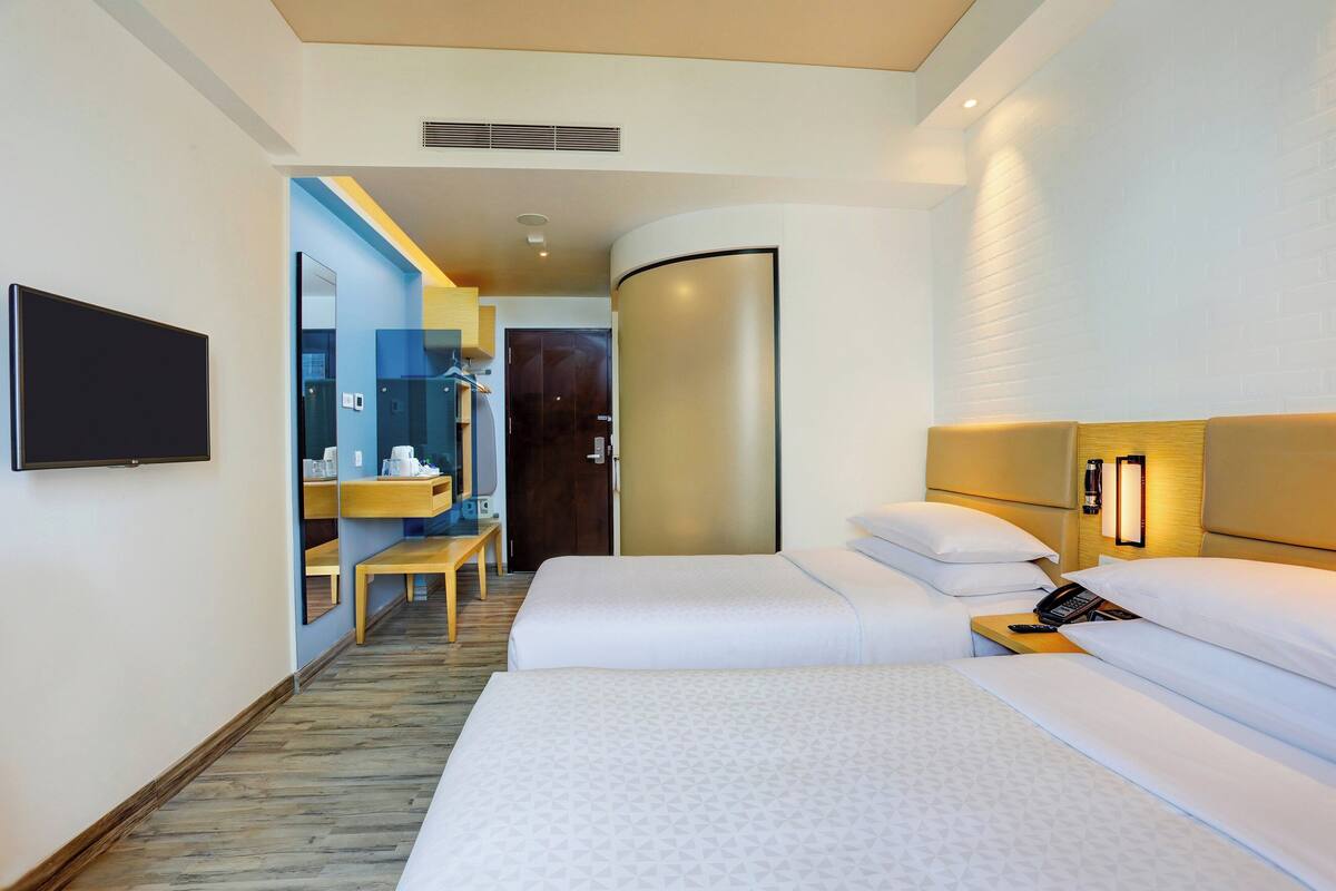 A hotel room with two beds, a TV, a bathroom with a mirror, and a small table.