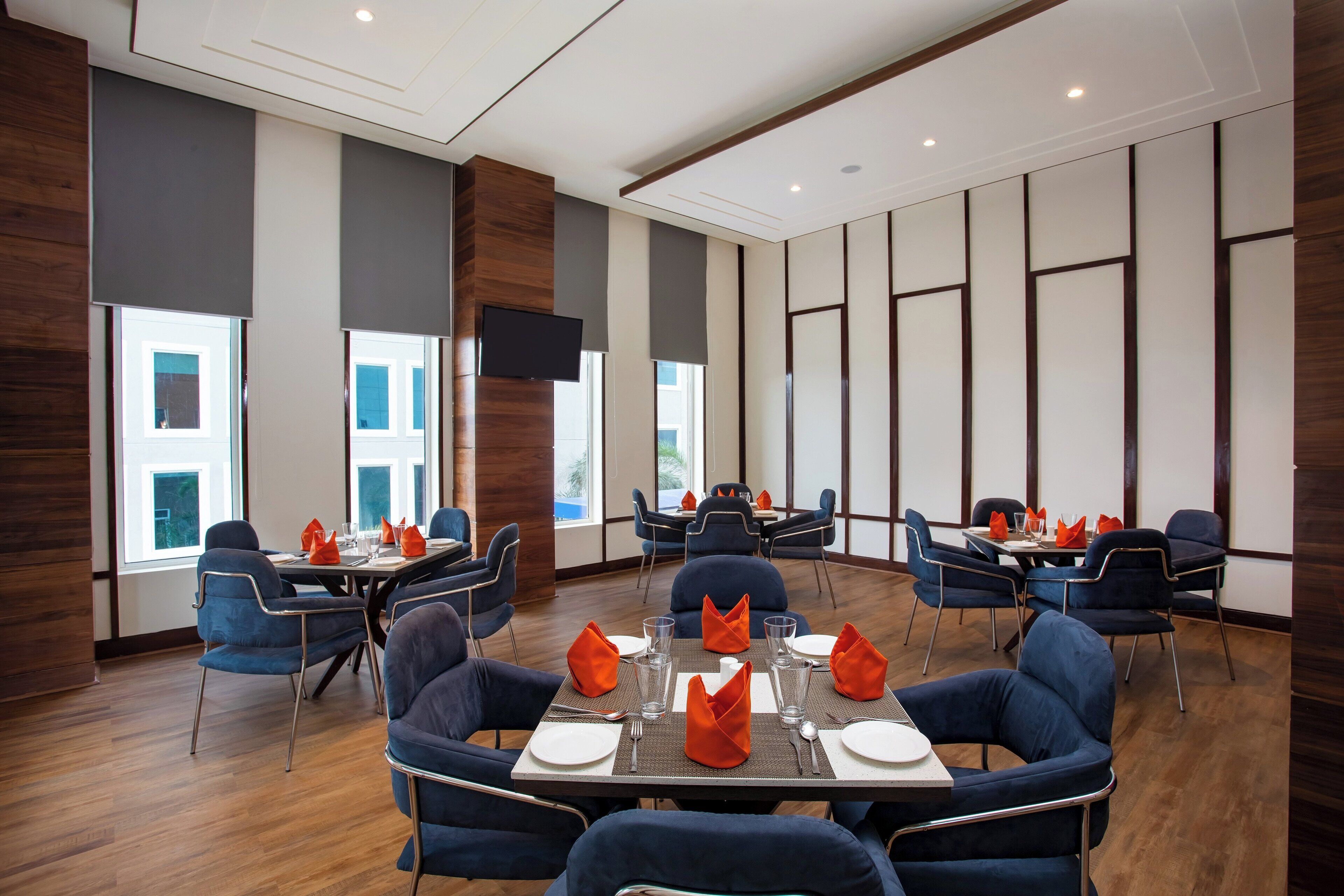 A modern dining area with round tables, blue chairs, and orange napkins.