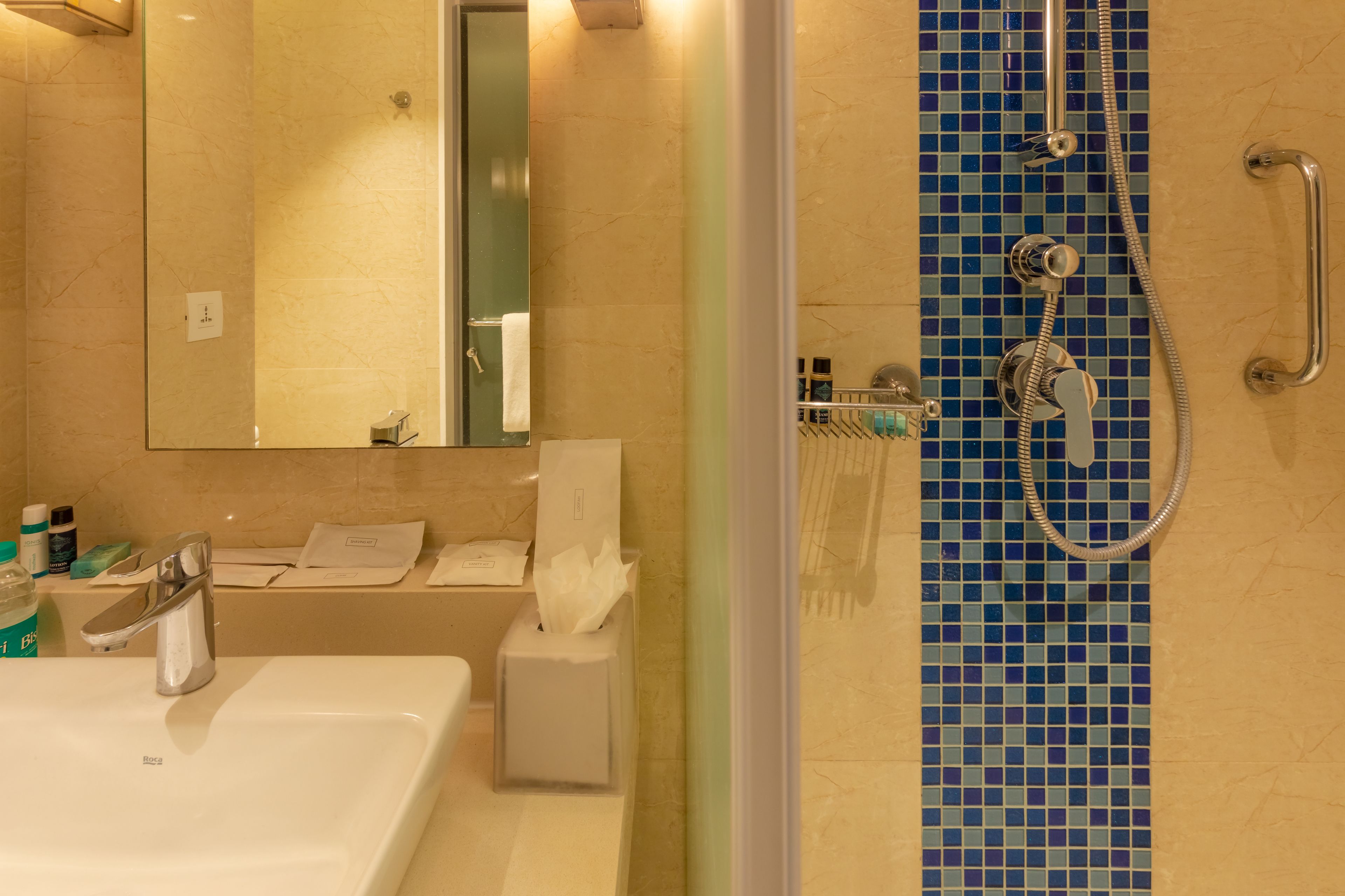 Baño con lavamanos, espejo, toallero y ducha con pared de mosaicos azules.