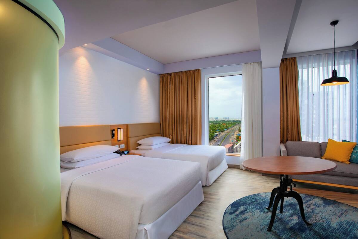 A hotel room with two beds, a sofa, a round table, and a view of the city.