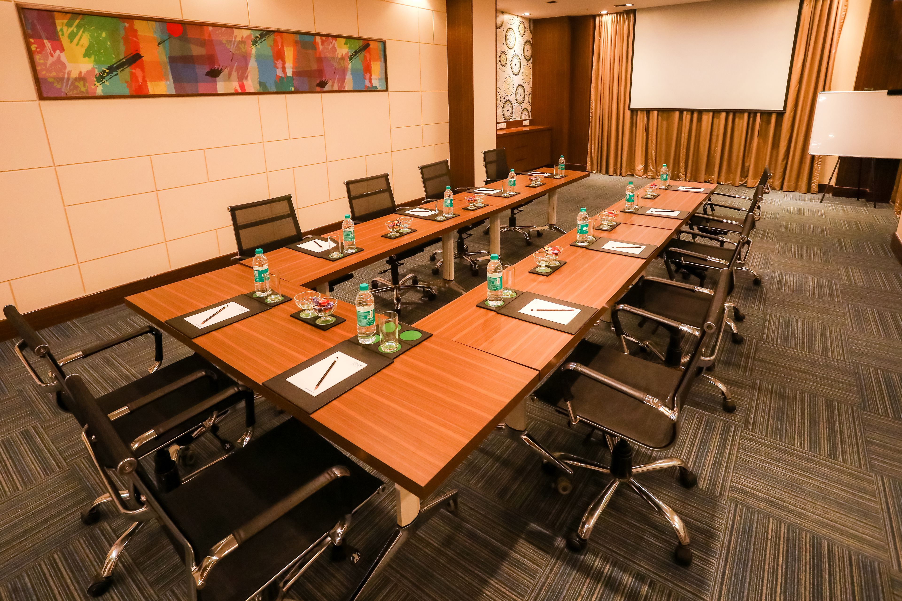 A conference room with a long table, chairs, water bottles, and a projector screen.
