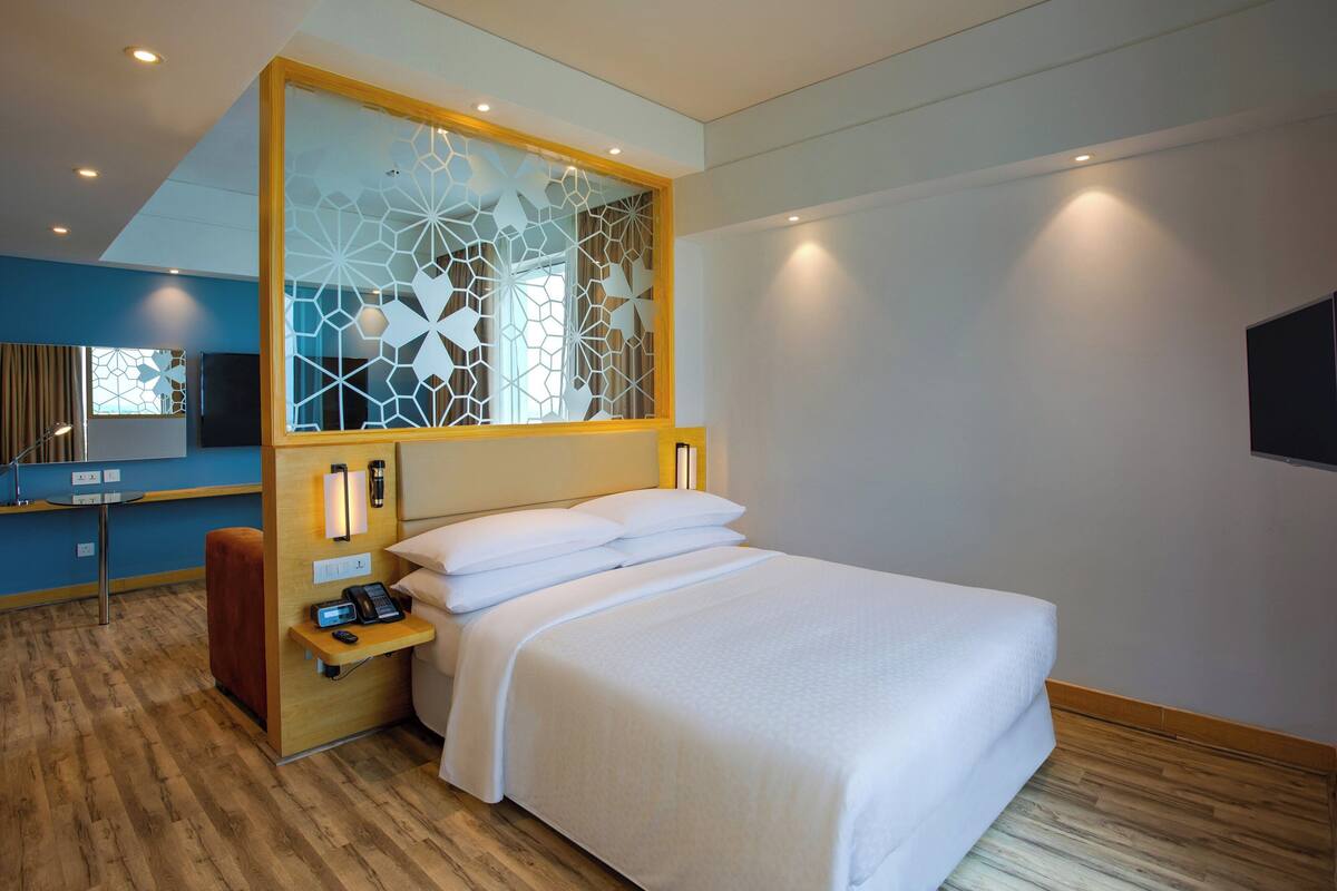A modern hotel room with a large bed, a bedside table with a phone and lamp, a decorative partition, and a television on the wall.