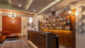 Un área de recepción moderna con un mostrador de madera, un sofá y una pared decorativa con relojes que muestran nombres de ciudades.