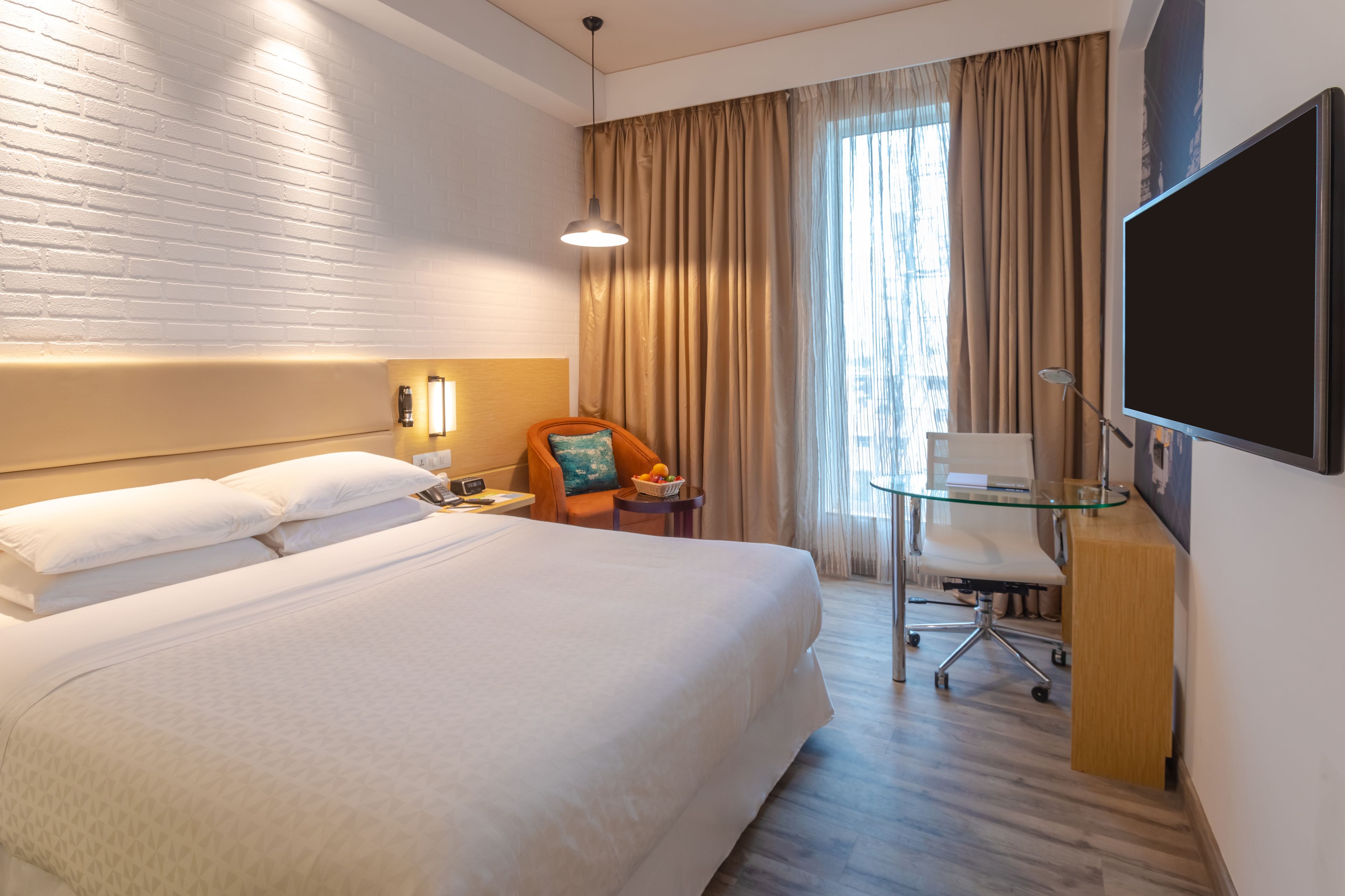 A hotel room with a large bed, a desk with a chair, a TV, and a window with curtains.