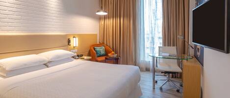 A hotel room with a large bed, a desk with a chair, a TV, and a window with curtains.