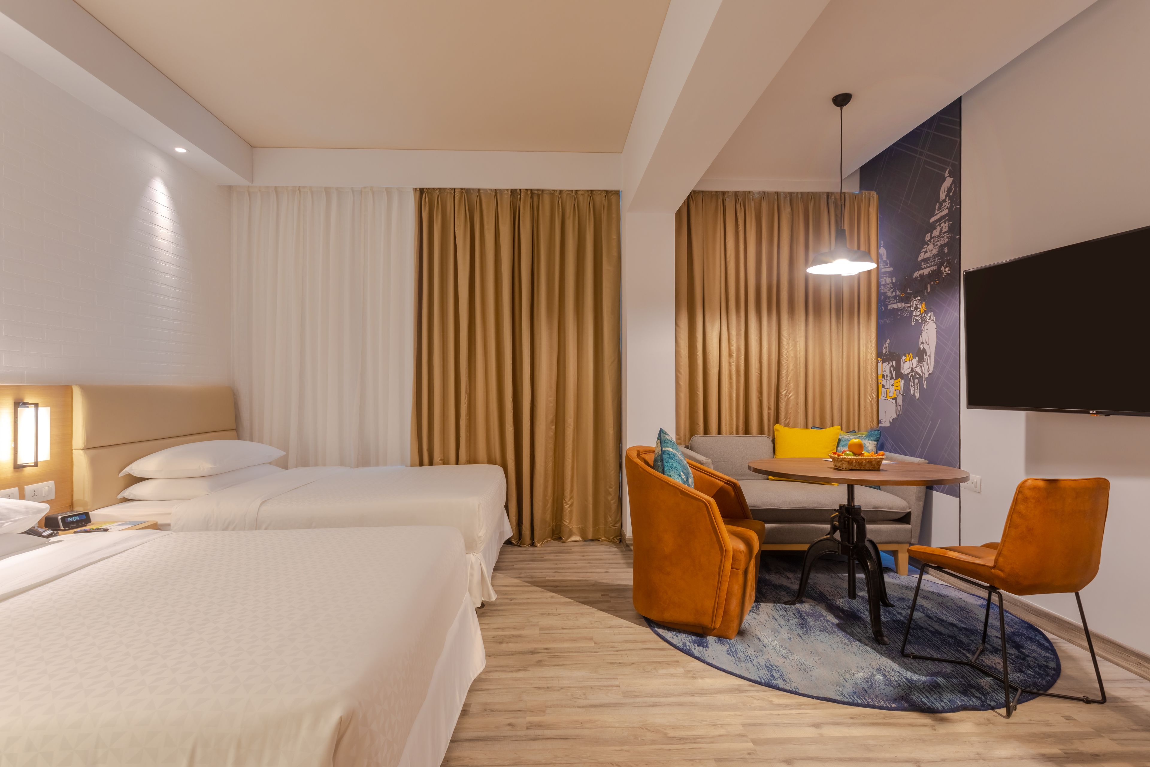 Une chambre d’hôtel avec deux lits, un coin repas comprenant une table et des chaises, et un grand téléviseur à écran plat fixé au mur.