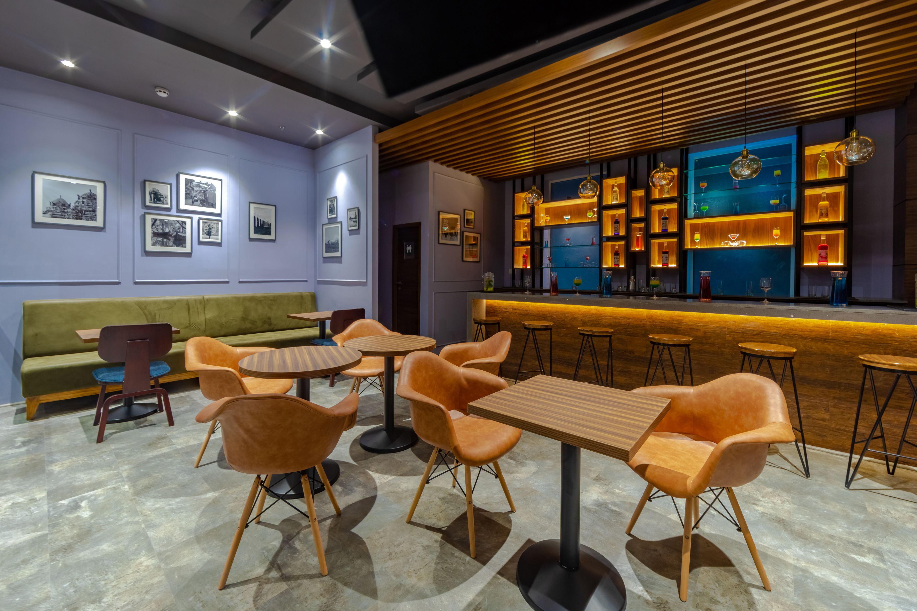 A modern bar area with wooden tables and chairs, a green sofa, and a wall with framed pictures.