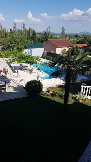 A pool area with a clear view of the pool, surrounding greenery, and a building in the background. - Holiday House Iva (Imotski)