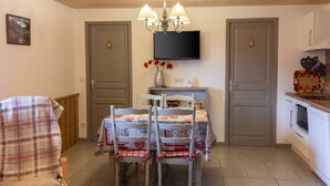 A dining area with a table set for four, a television above the table, and a kitchen area to the right. - Homerez - Apartment in Cornimont (Cornimont)