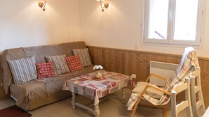 A cozy room with a sofa, a table with a patterned tablecloth, a chair, and two wall-mounted lamps. - Homerez - Apartment in Cornimont (Cornimont)