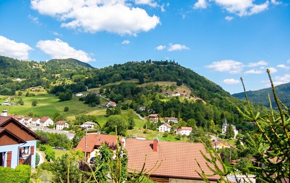 A rural village with houses on a hillside, surrounded by greenery and a clear sky.