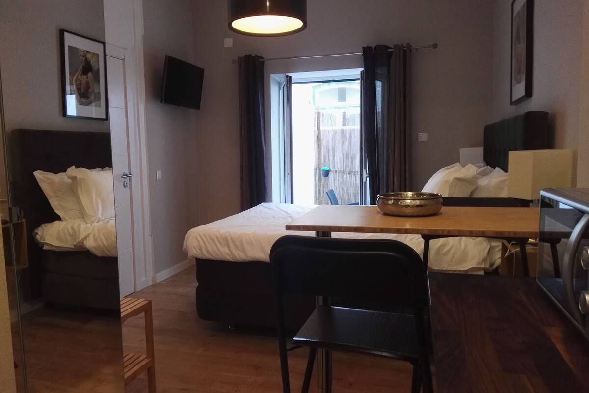 A compact hotel room with a bed, a small table, a chair, a TV, and a window with curtains.