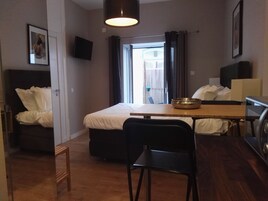 A compact hotel room with a bed, a small table, a chair, a TV, and a window with curtains.