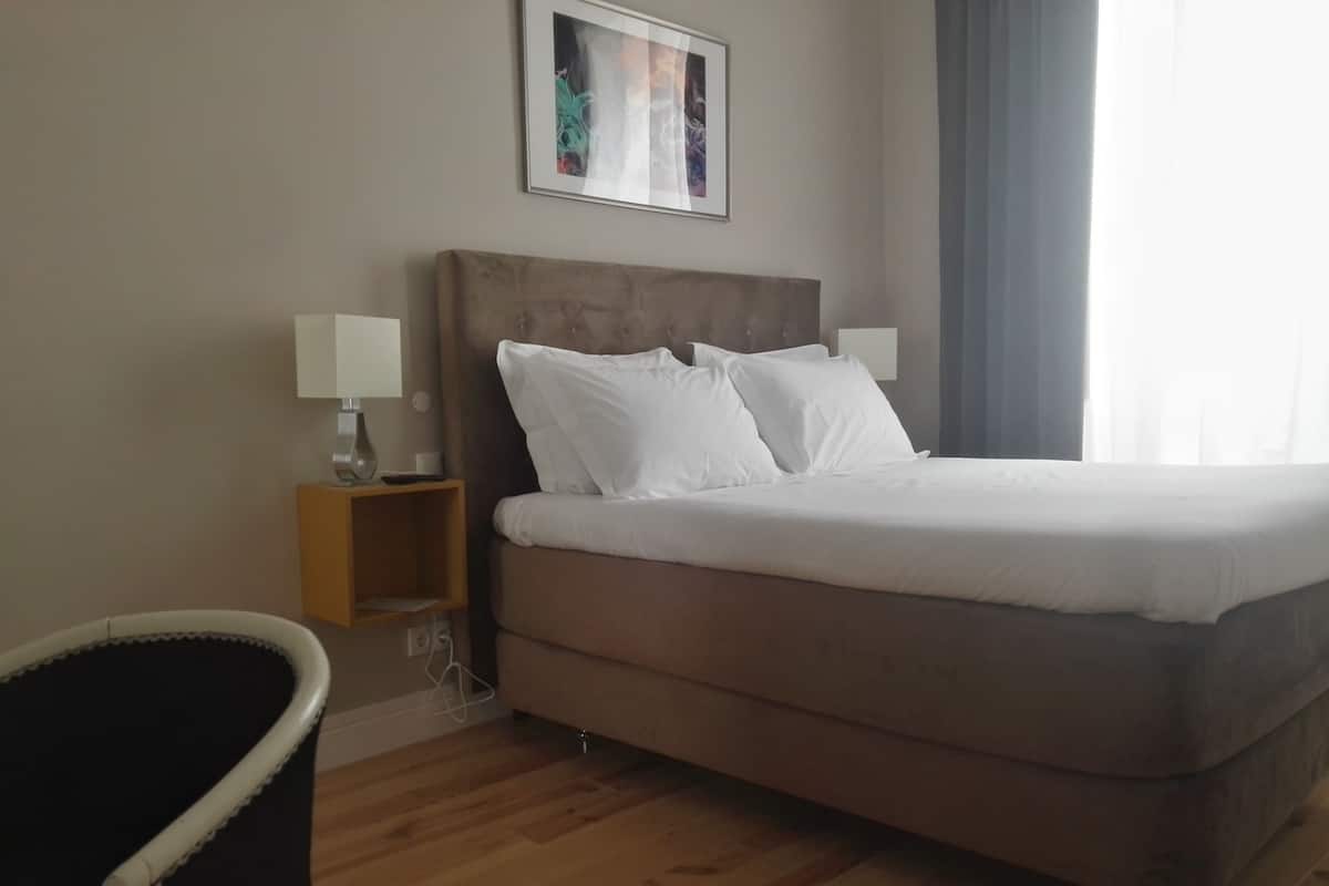 A bedroom with a large bed, two bedside tables with lamps, a chair, and a painting on the wall.